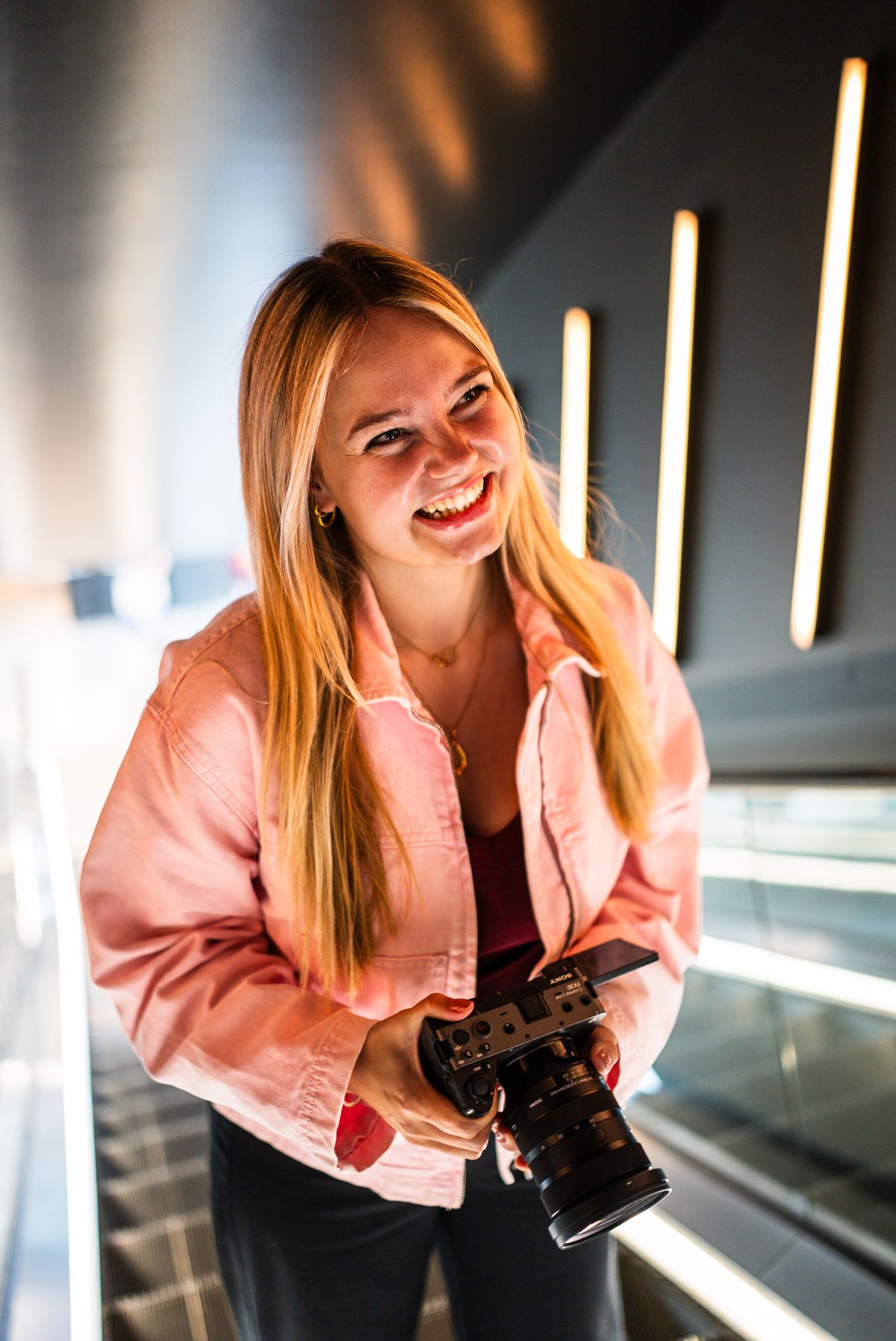 Martine met haar filmcamera op de verlichte roltrap, lachend.